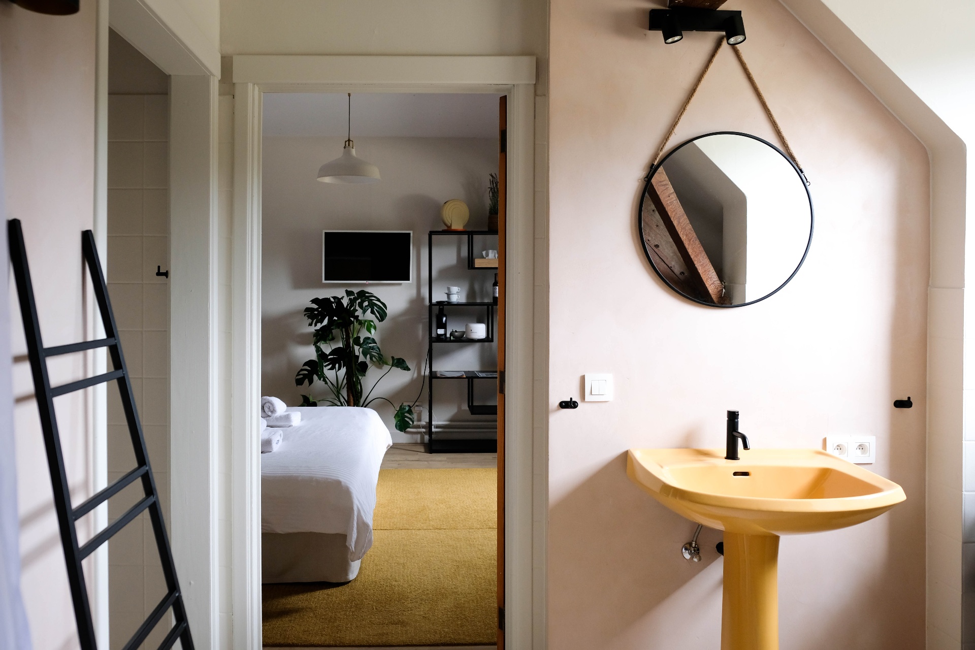 Slaapkamer met okergele wastafel en ronde spiegel